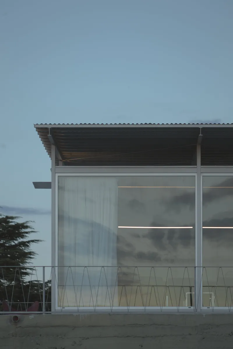 Corner detail of translucent polycarbonate wall with metal railing under corrugated roof overhang at twilight