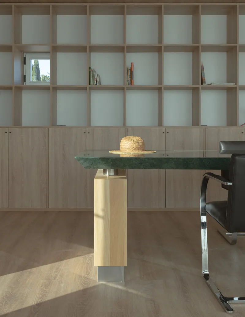 Floor-to-ceiling timber bookshelf with lower cabinets behind a green stone table with timber and metal base