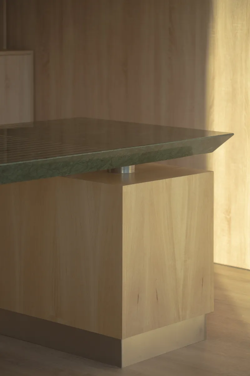 Close-up of green stone tabletop cantilevered over timber pedestal base in warm afternoon light