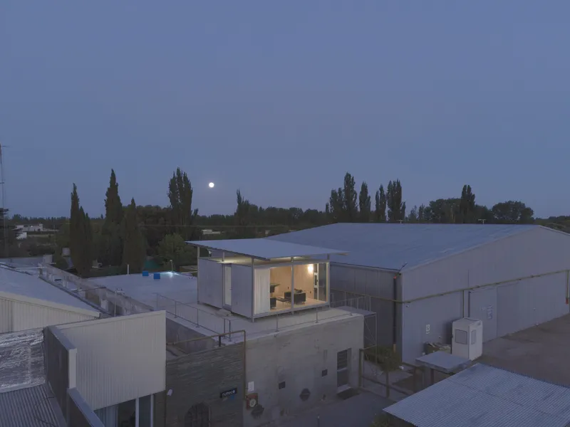 Elevated rooftop pavilion with glass walls and timber cladding at dusk with moon rising