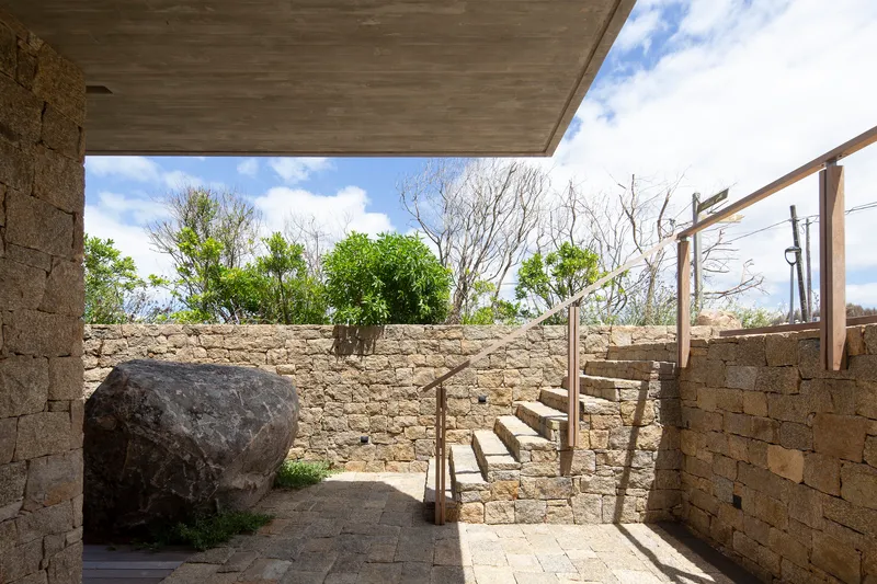 Outdoor courtyard with stone walls, a large boulder, and timber staircase under a concrete soffit