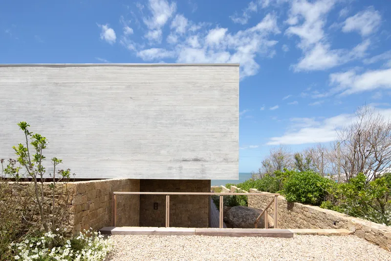Concrete upper volume cantilevered above a recessed stone base with distant ocean views