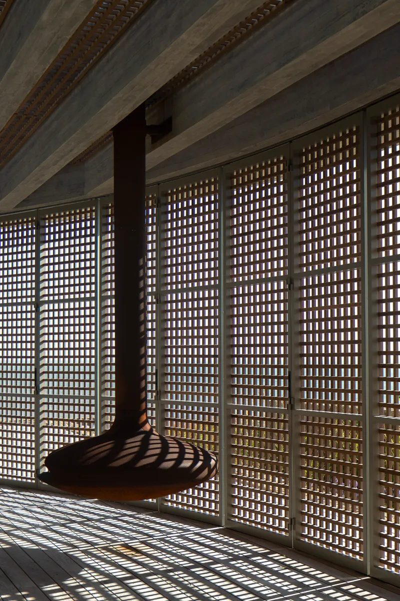Corner view of the timber lattice wall filtering light onto a suspended daybed beneath exposed concrete beams