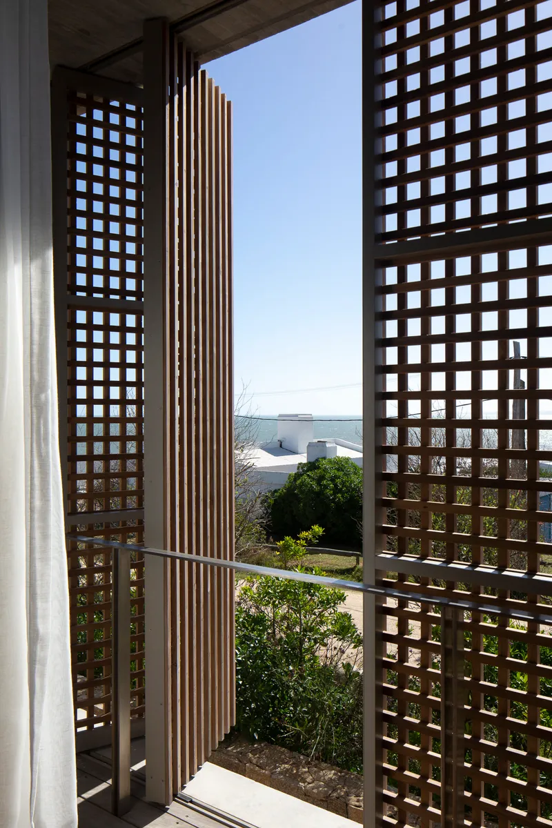 Interior view through the lattice screen opening to a planted courtyard with ocean beyond