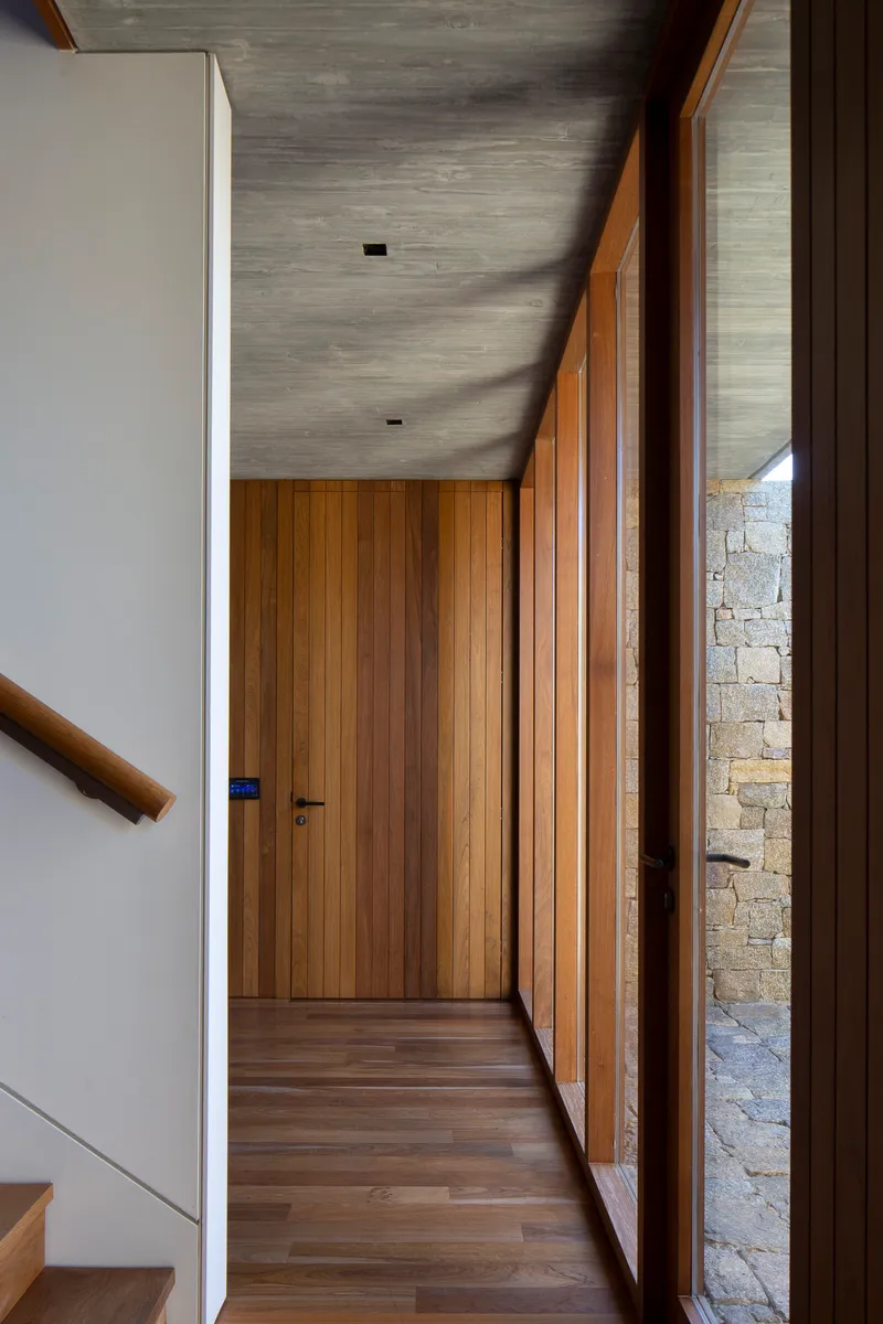 Corridor with board-marked concrete ceiling and timber-lined walls framing a view to the stone wall