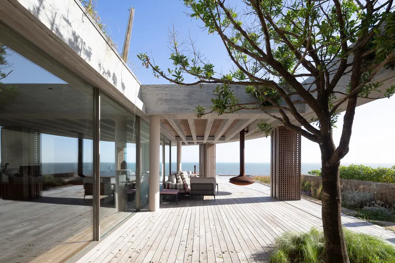 Open concrete pavilion with exposed beams sheltering a timber deck with ocean views beyond