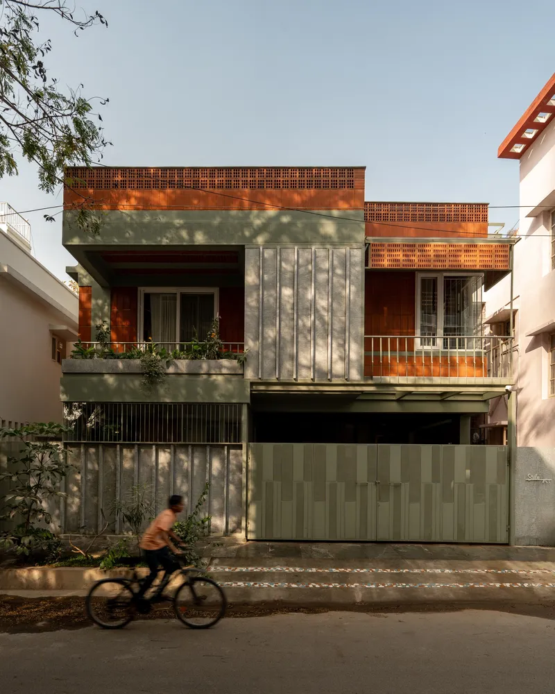 Street facade with vertical concrete panels and perforated brick screens as a cyclist passes in afternoon light