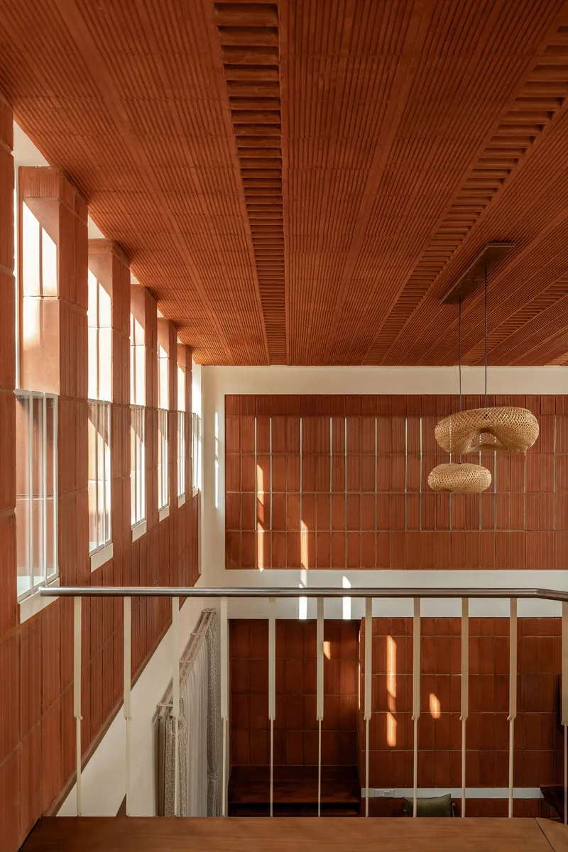 Double-height atrium with timber-slatted ceiling and wall panels flooded with afternoon sunlight