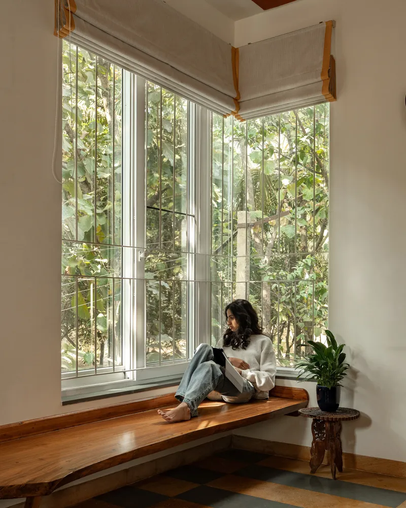 Corner window seat with live-edge timber platform overlooking a lush planted courtyard