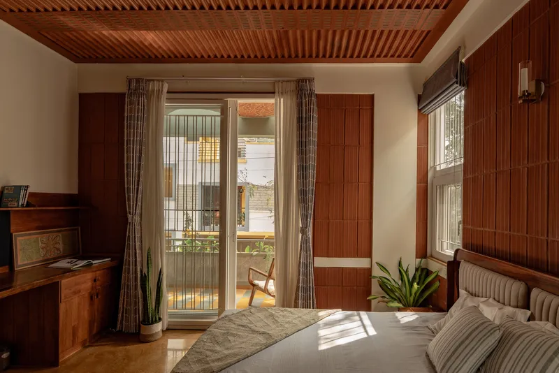Bedroom with slatted timber ceiling and walls opening to a balcony with afternoon sun