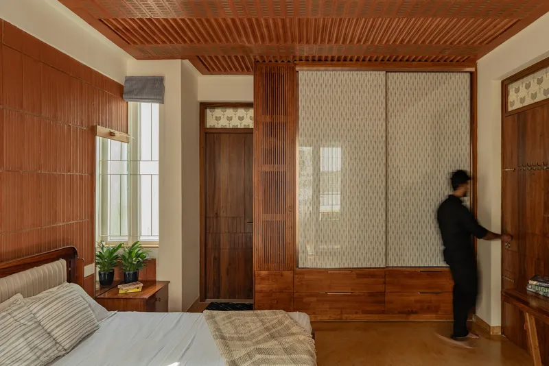Bedroom with timber slatted ceiling and built-in wardrobes with woven screen panels as figure approaches door