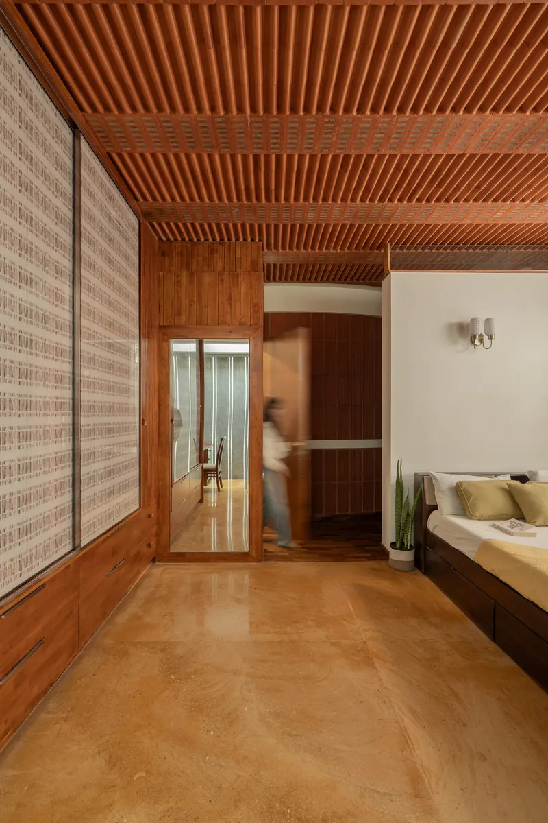 Hallway with exposed timber beam ceiling and woven screen wall panels as figure passes doorway