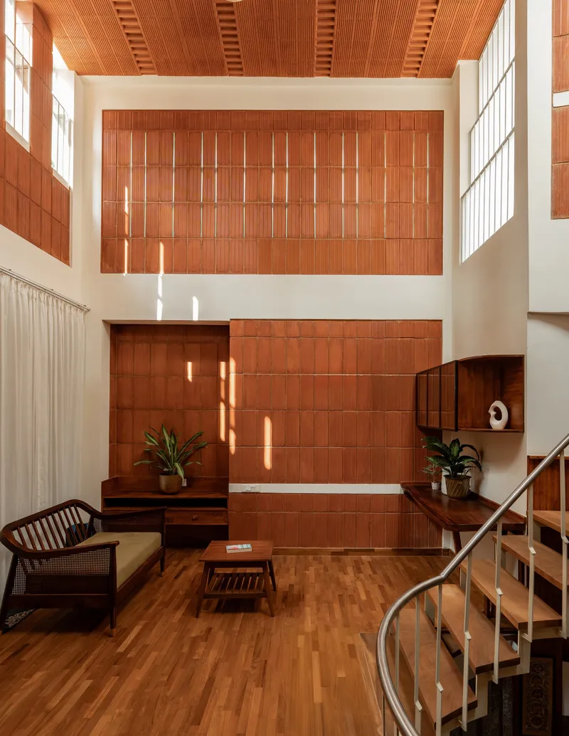 Double-height living room with terracotta tile wall and slatted timber ceiling in afternoon sun