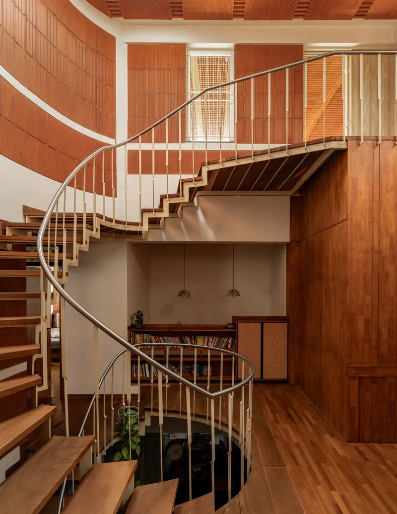 Open timber treads of the helical stair wrapping around a circular void with hanging plants
