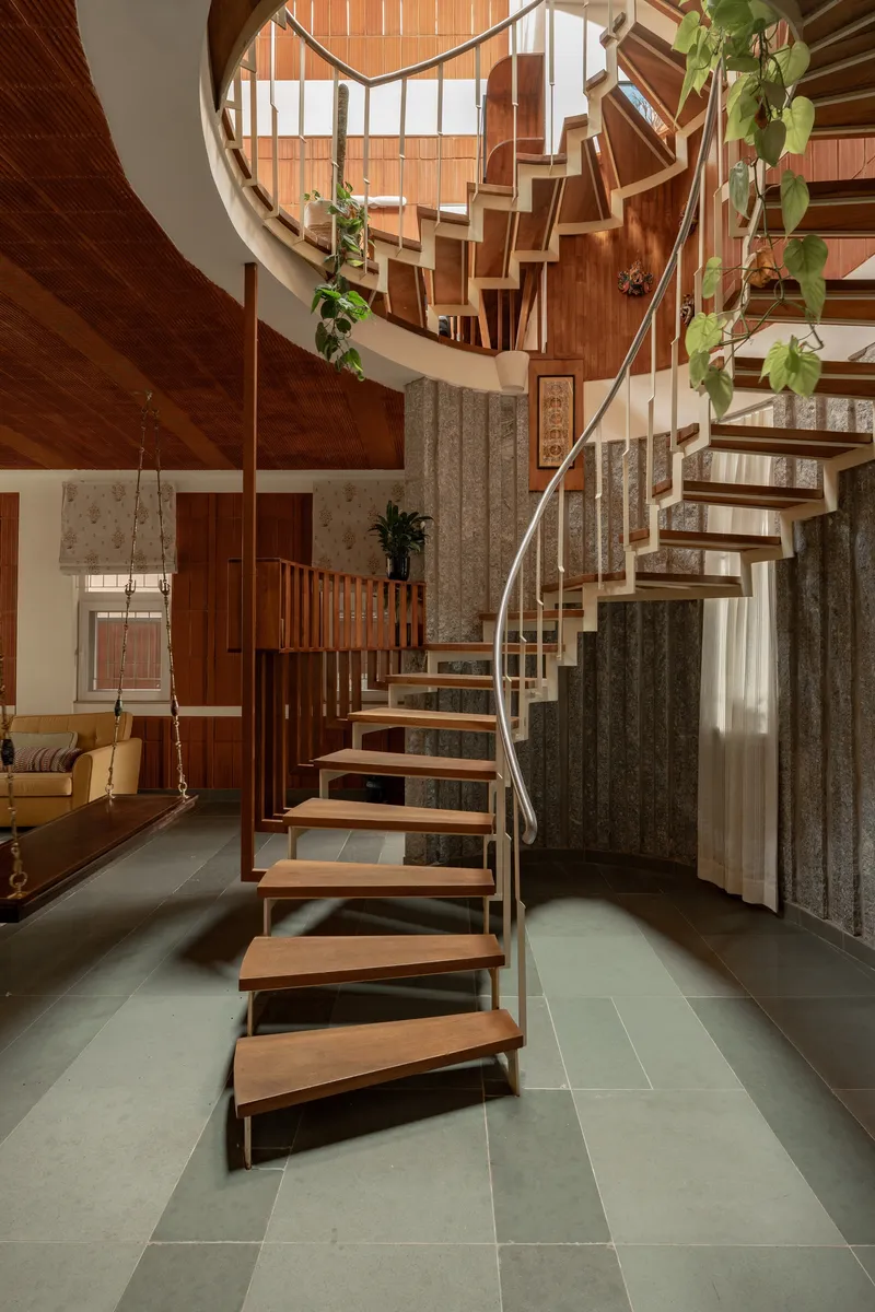 View from below showing the spiral stair rising from grey tile flooring with trailing greenery