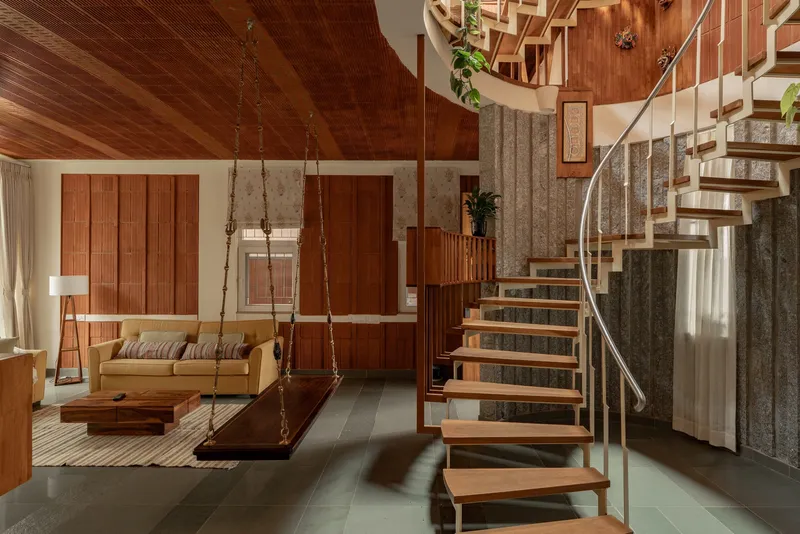 Living area with suspended wood swing bench and spiral stair under a timber-clad vaulted ceiling