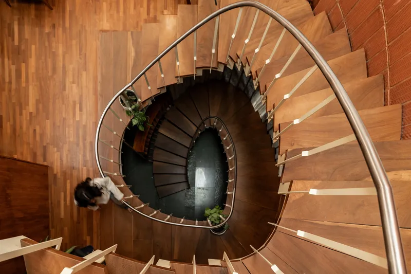 Overhead view of a spiraling timber staircase with steel handrail and a person descending
