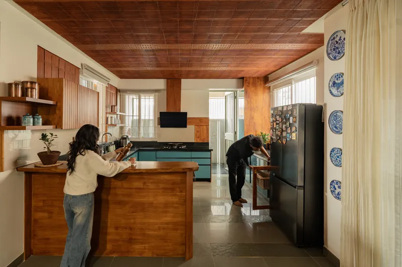 Kitchen with timber island and slatted wood ceiling occupied by two people preparing food