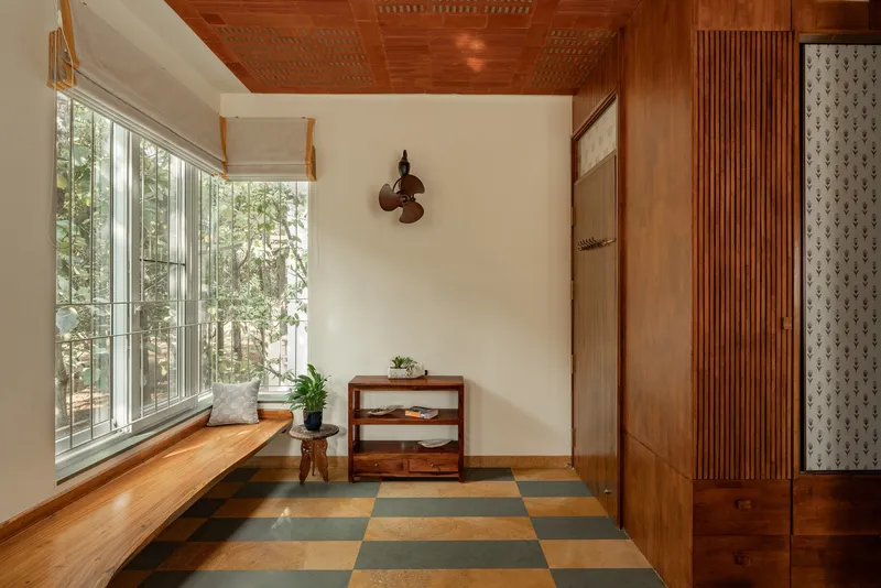 Entrance nook with built-in timber bench, checkered floor tiles and garden view through tall windows