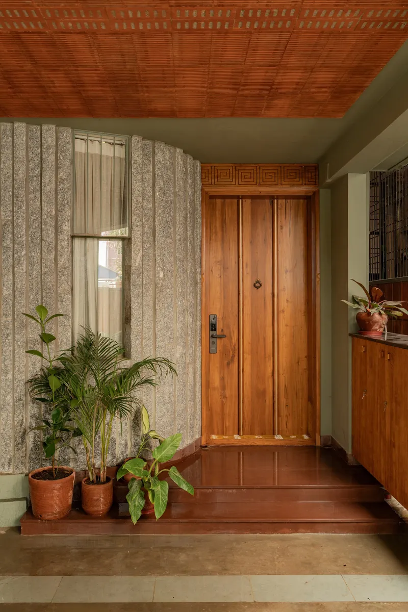 Entry foyer with carved timber door, patterned stone wall and potted plants on terracotta tiles