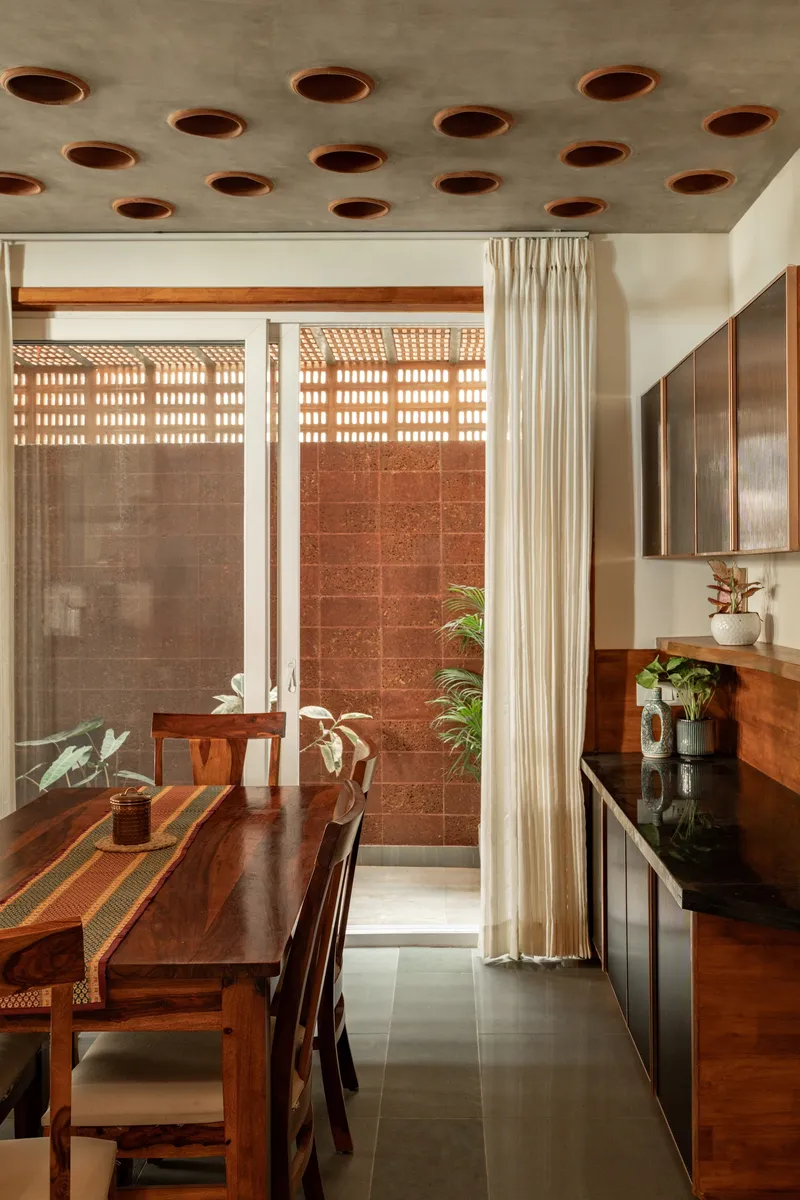 Dining area with perforated concrete ceiling opening to courtyard with terracotta tile wall and plants