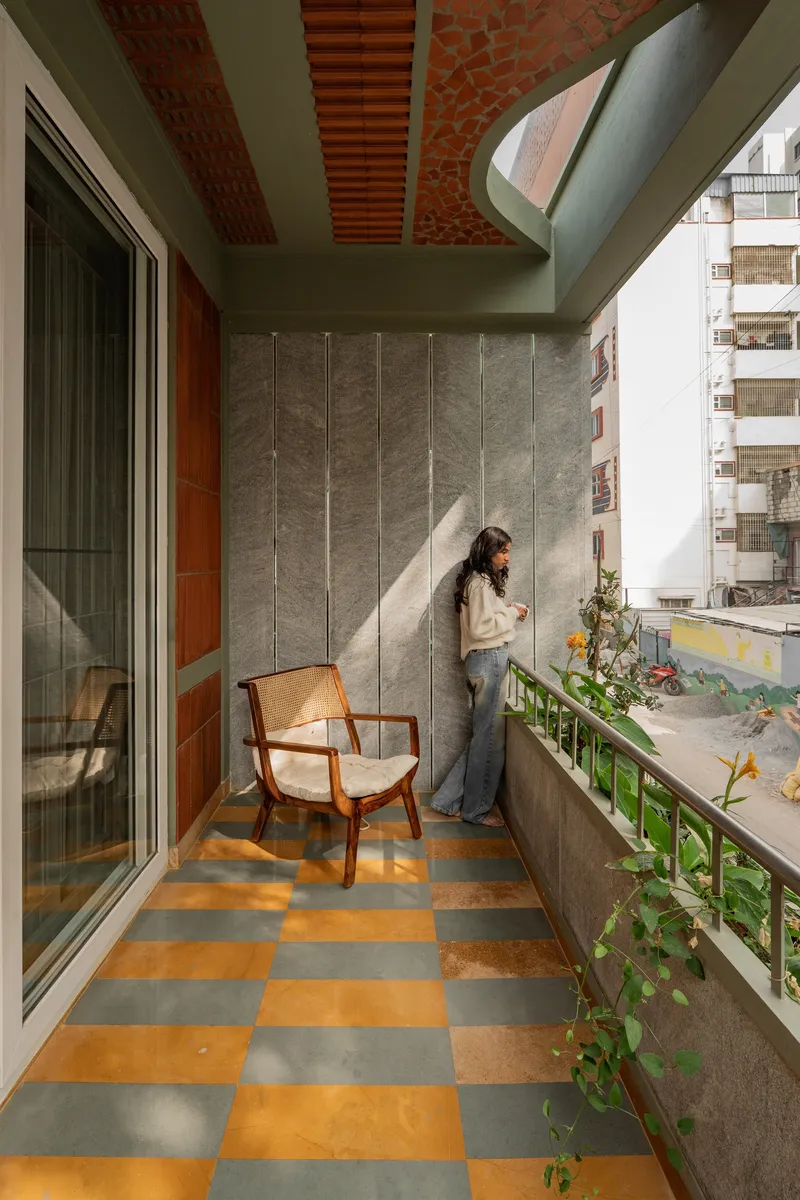 Balcony with chequered orange and grey floor tiles and brick ceiling panels as a resident leans against the wall