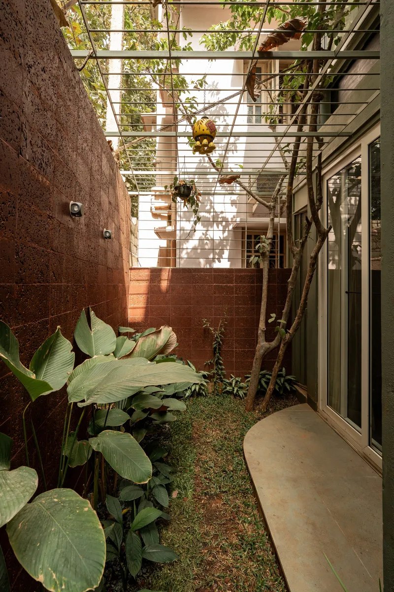 Narrow courtyard with red brick walls, a steel trellis overhead, and tropical plants below dappled afternoon light