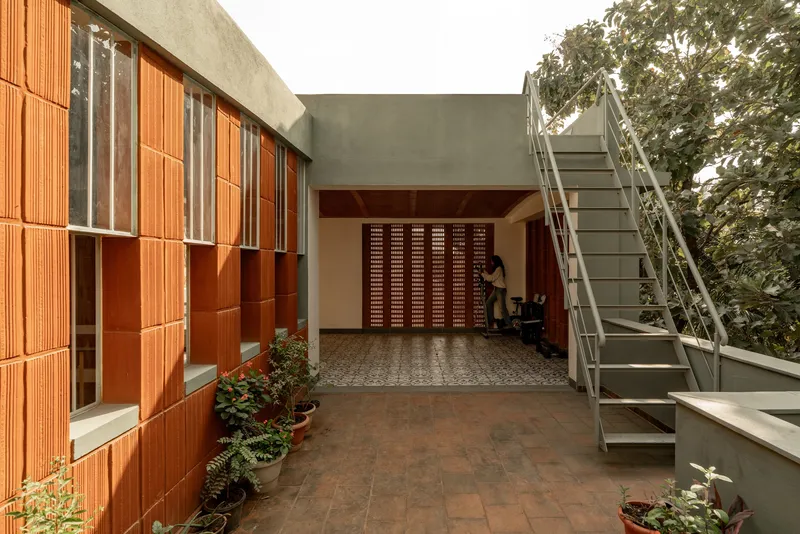 Covered entry terrace with red terracotta tile walls, a perforated screen door, and a steel stair to the upper level