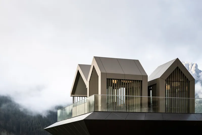 Cluster of three gabled volumes with vertical slat screens on a metal plinth in fog