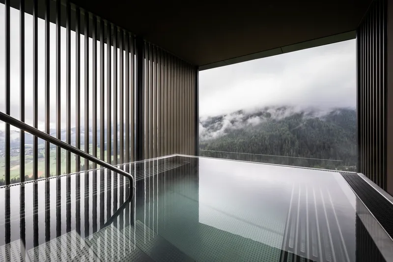 Interior pool with vertical slat screens and corner window framing forested mountains in low cloud