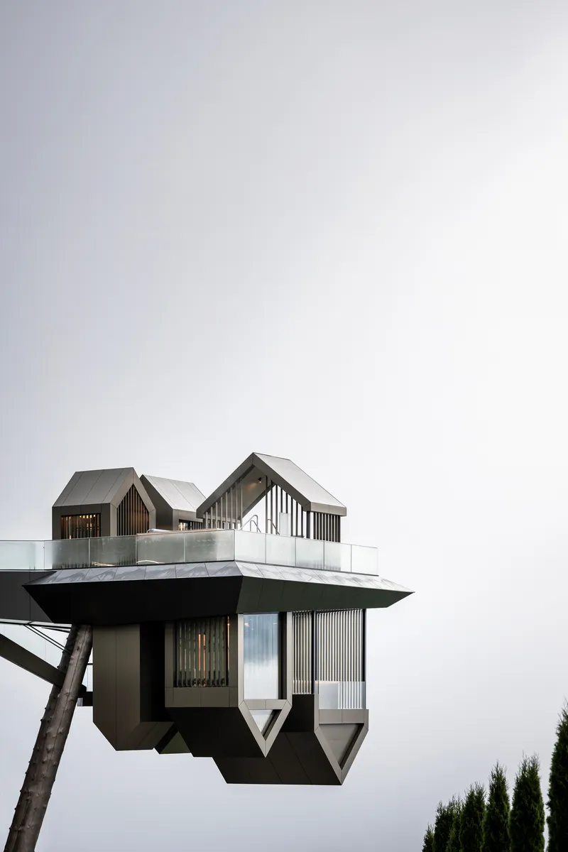 Elevated observation structure with gabled roof forms and vertical timber cladding against an overcast sky