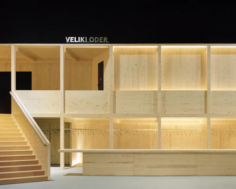 Two-story lobby with laminated timber walls, openings to upper level and illuminated grid ceiling at night