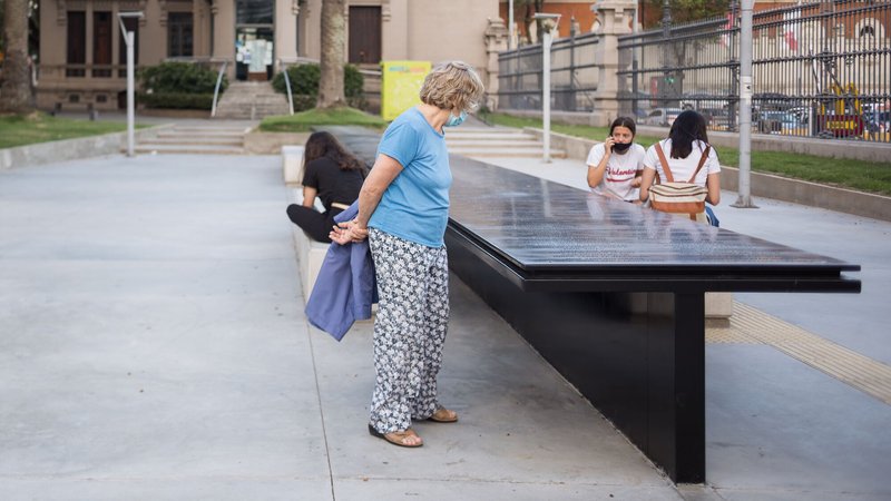 Visitors gathered around the black metal memorial table with inscribed surface in daylight