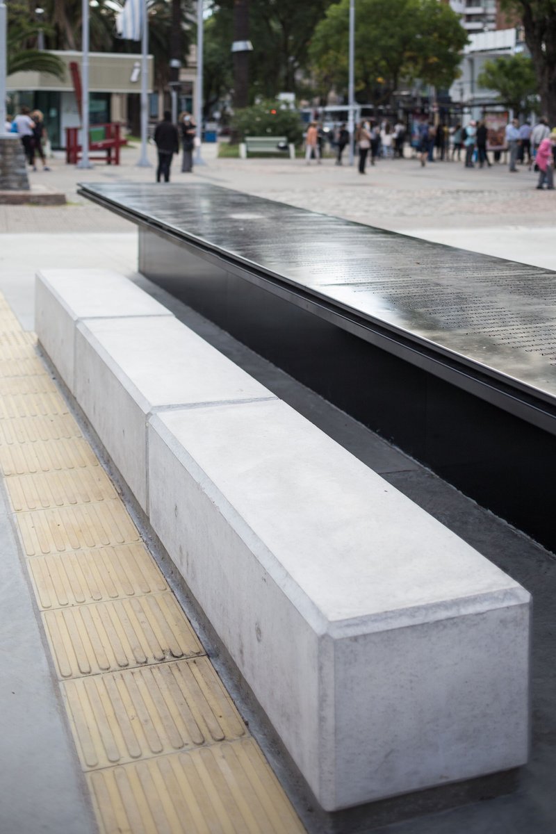 Detail of the black metal table edge meeting concrete bench seating and tactile paving strip