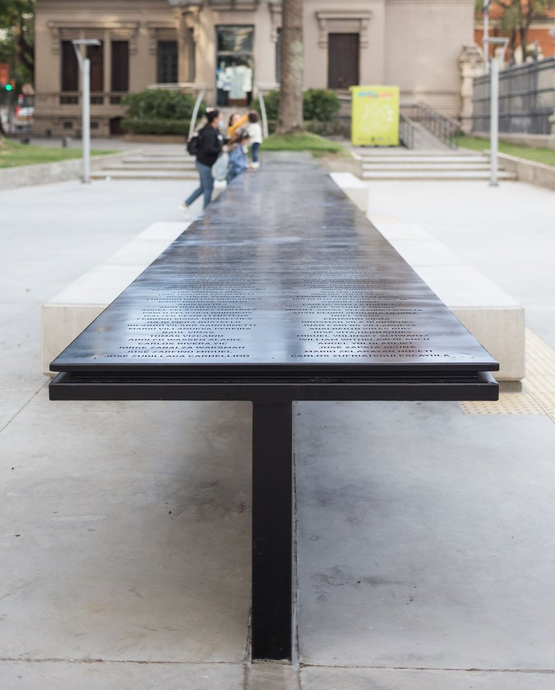 End view of the black steel memorial table with central support column and two pedestrians passing