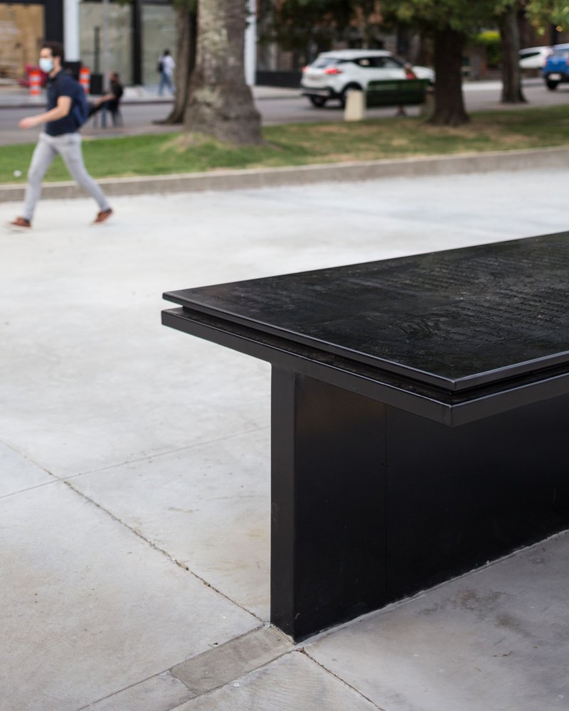 Black granite memorial bench with engraved surface in a public plaza with a pedestrian crossing