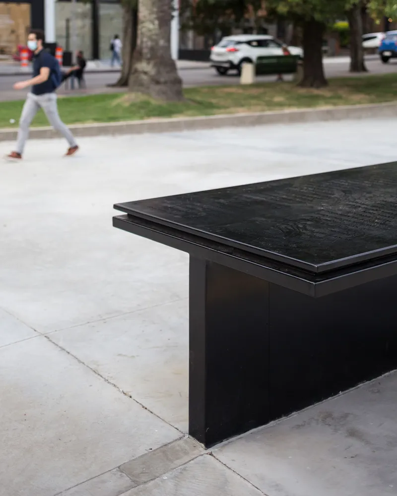 Black granite memorial bench with engraved surface in a public plaza with a pedestrian crossing