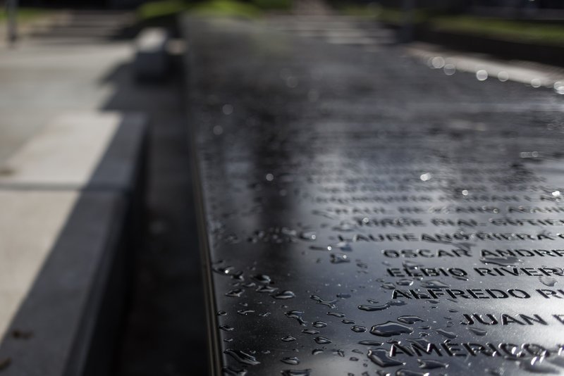 Close-up of engraved names on wet black granite surface with water droplets
