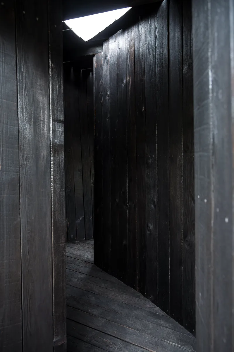 Dark timber interior corridor with triangular skylight casting bright daylight through the opening above