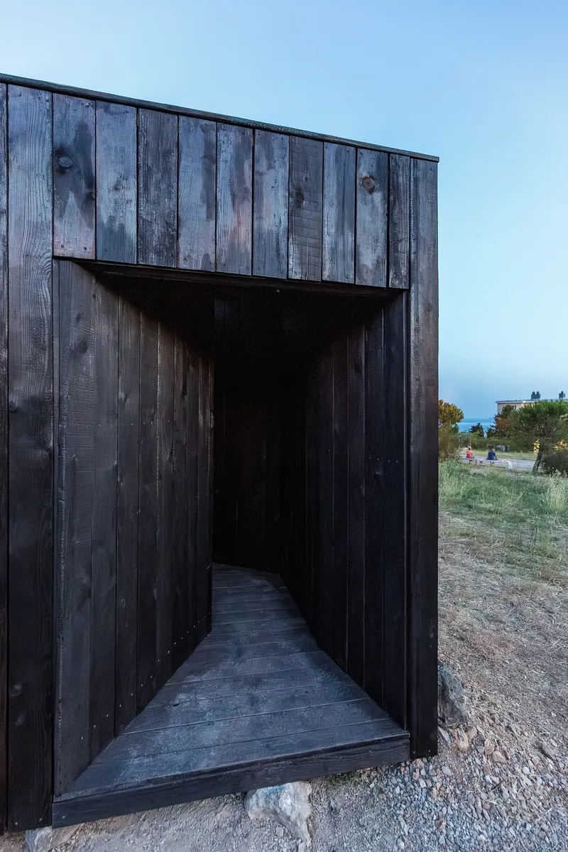 Recessed entrance through blackened timber walls leading to a dark interior corridor at dusk