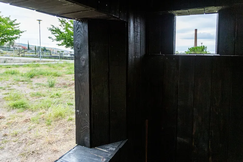 Interior threshold space with charred timber walls framing horizontal window openings to the landscape
