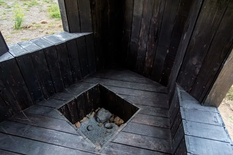 Top-down view of a square floor opening with stones below and charred timber bench surround