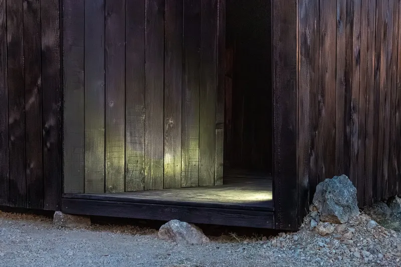 Doorway through charred wood walls revealing an illuminated interior passage with stone at base