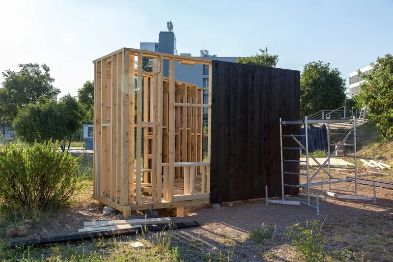 Partially enclosed pavilion showing light timber framing alongside charred vertical wood siding in afternoon sun