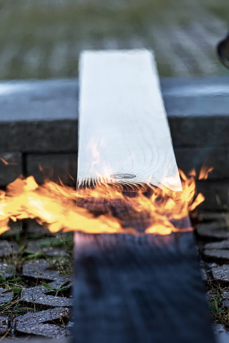 Timber plank being flame-treated with active fire charring the wood surface