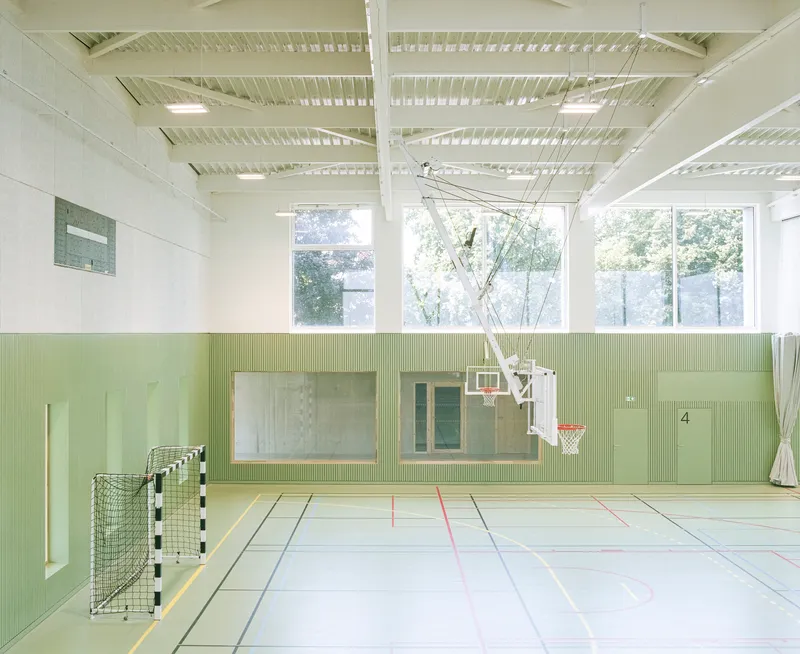 Sports hall with pale green ribbed wall panels and high windows overlooking exterior trees