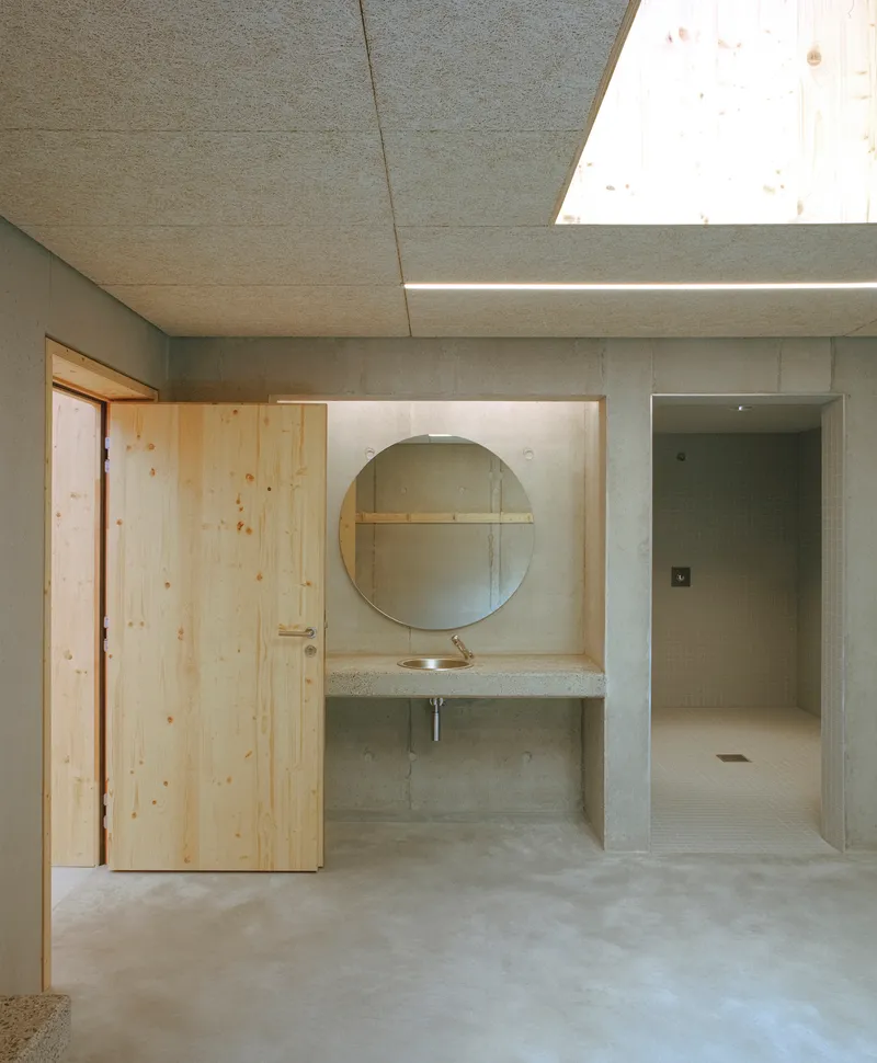 Changing room corridor with concrete sink niche, round mirror and skylight above timber door