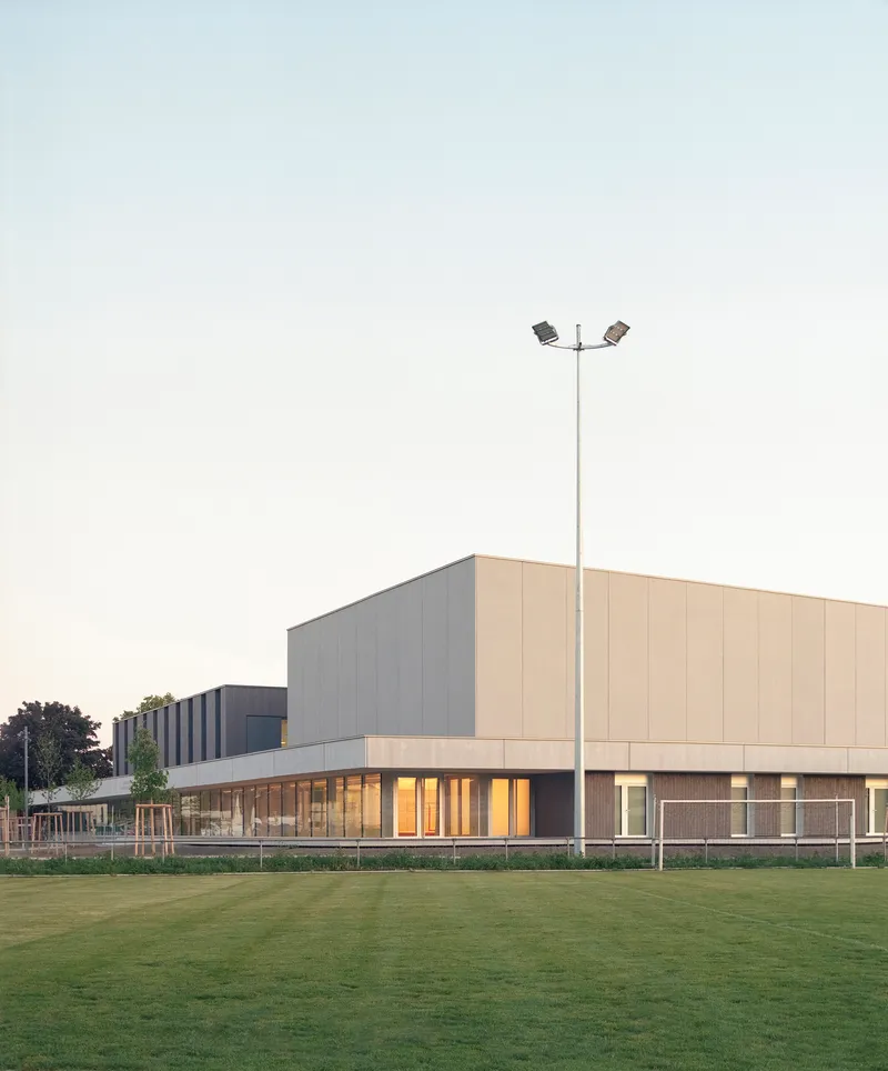 Stacked volumes with vertical ribbed panels and horizontal glazing strip viewed across lawn with light pole
