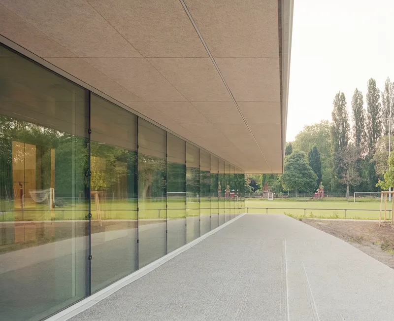 Covered walkway with continuous glazing reflecting sports field and trees beyond under fibrous ceiling panels
