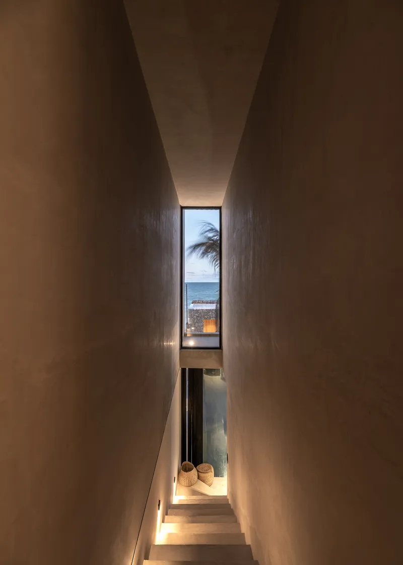 Narrow staircase with polished concrete walls and vertical window framing palm and ocean